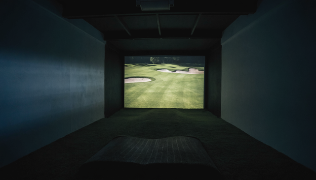 Golf simulator room at night with a course projected across the impact screen