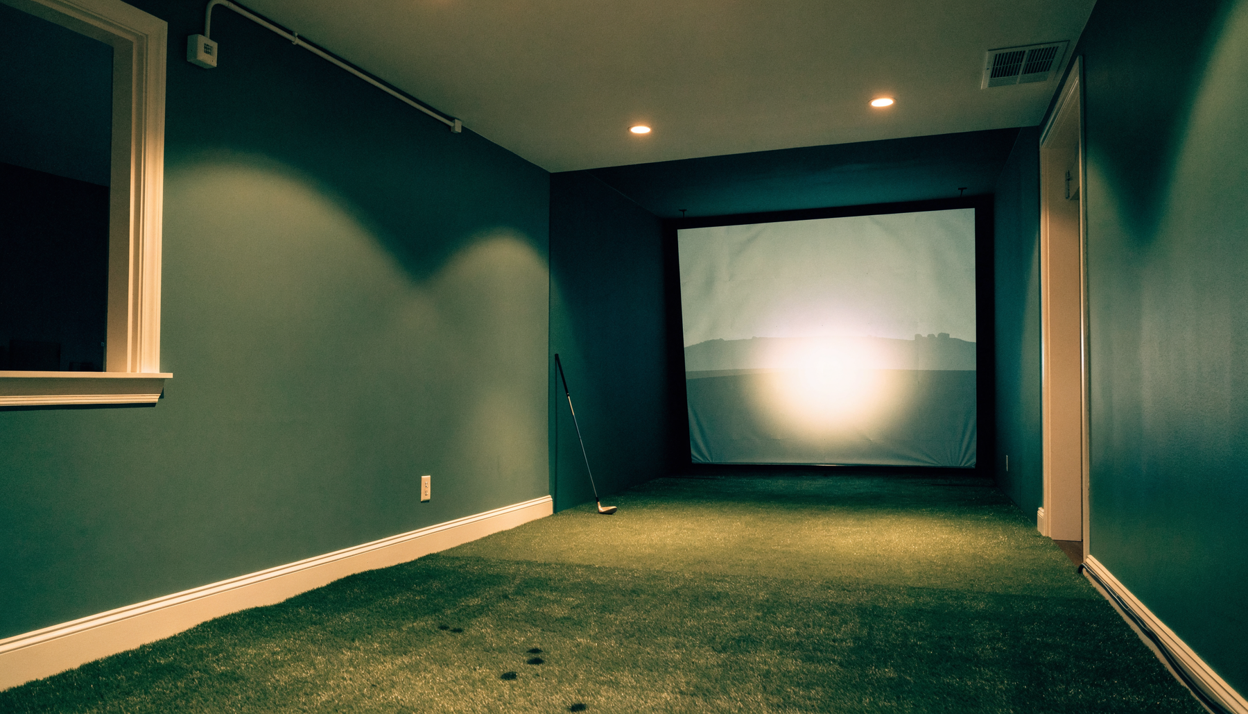 Finished home golf simulator room with impact screen and turf hitting mat