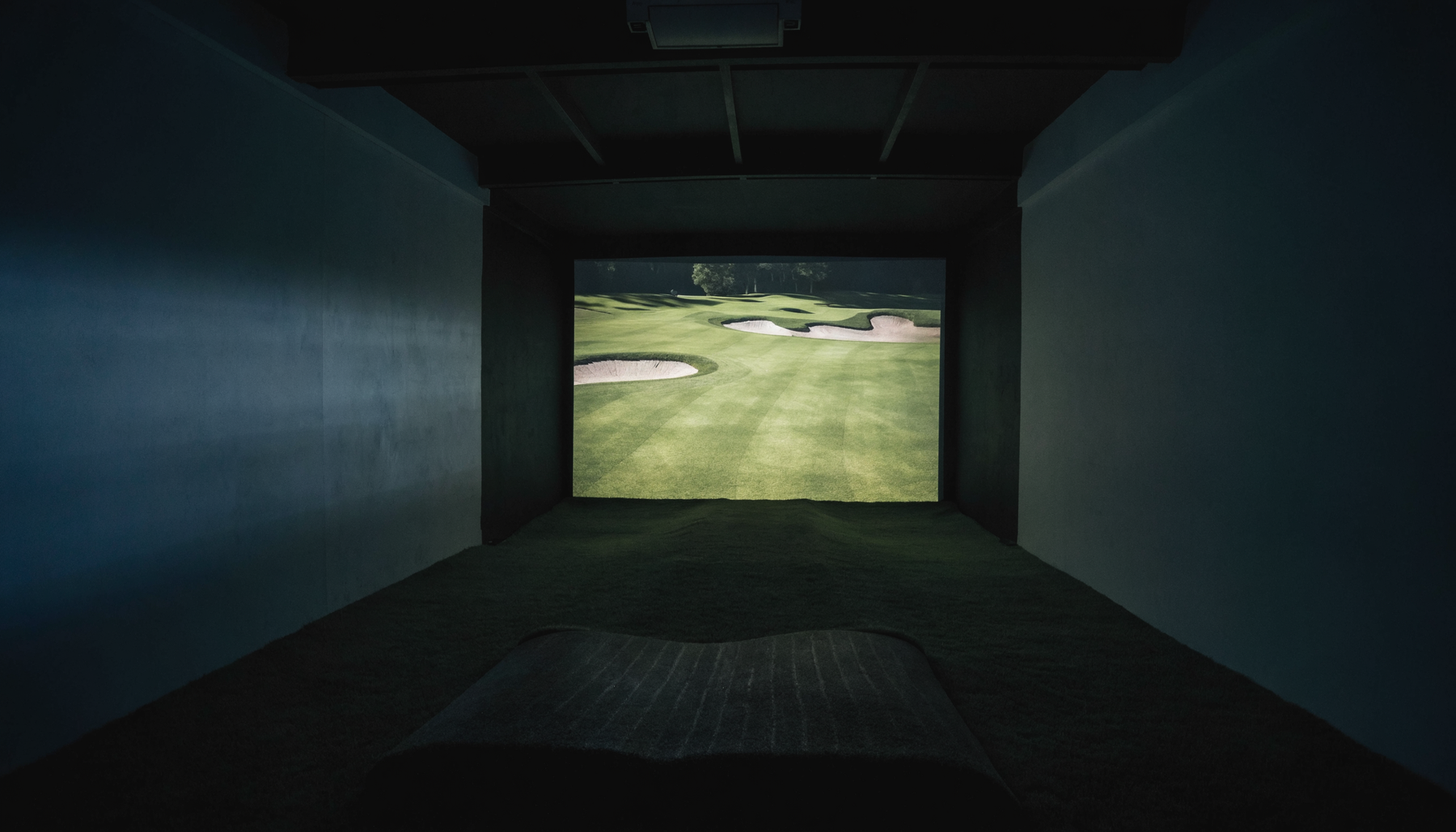 Golf simulator room at night with a course projected across the impact screen