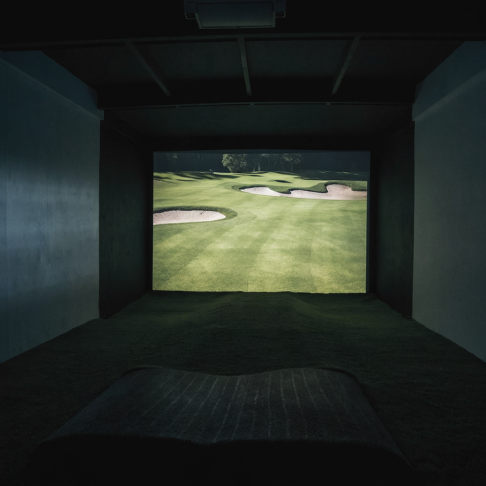 Golf simulator room at night with a course projected across the impact screen