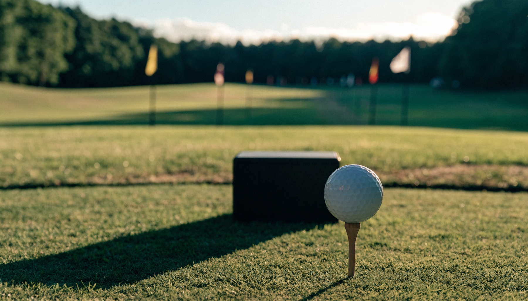 Outdoor grass driving range at golden hour with a golf ball teed up in the foreground