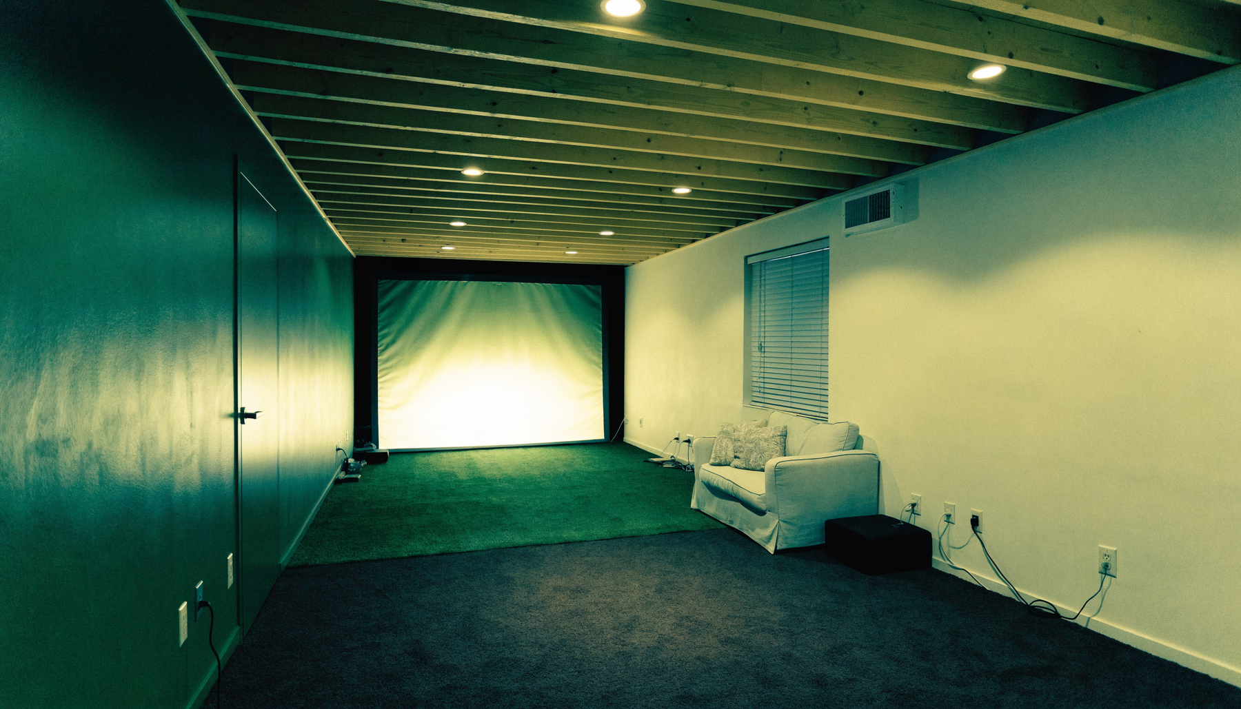 Finished basement golf simulator room with low ceiling and exposed painted joists