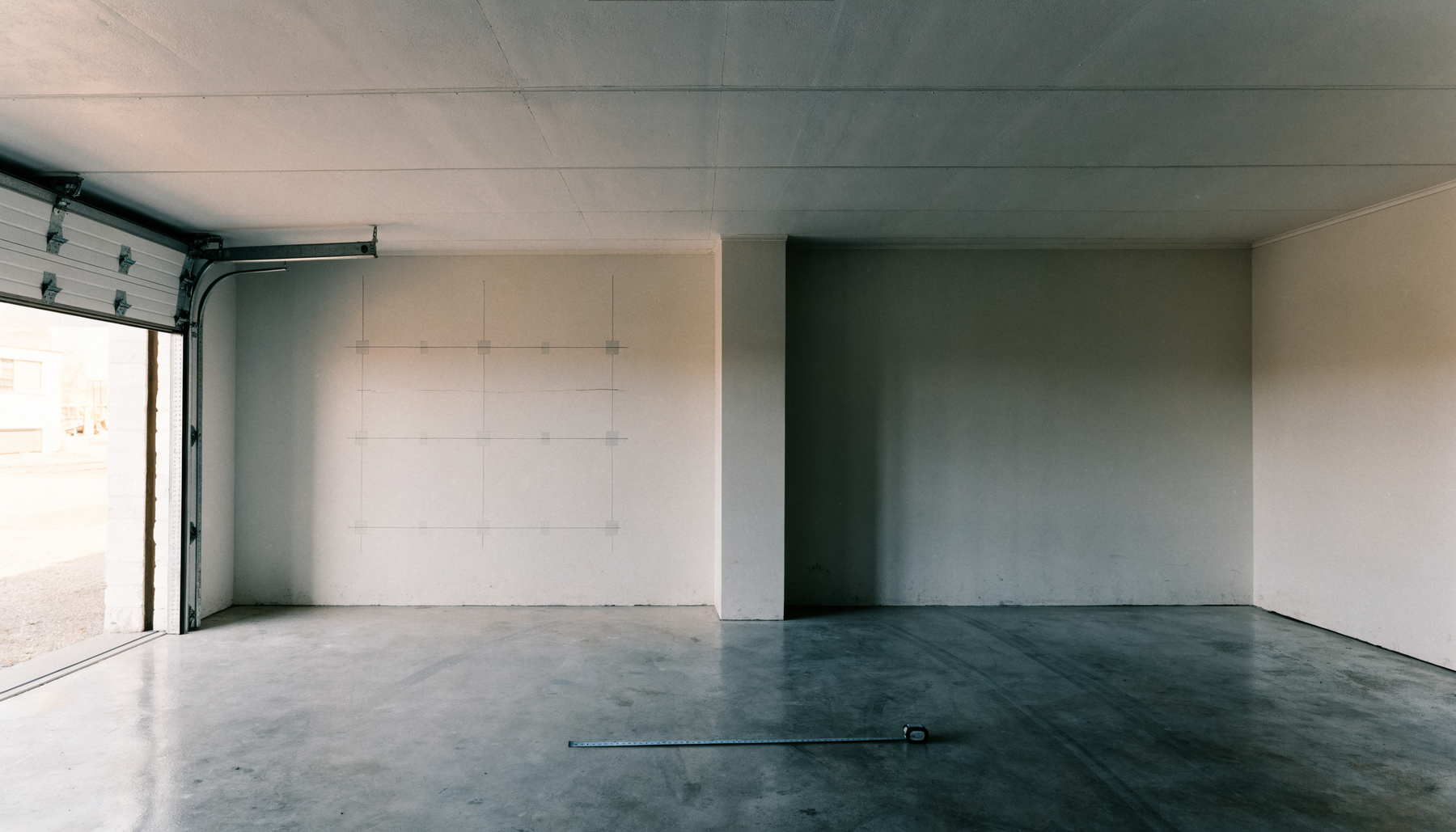 Empty two-car garage with a tape measure on the floor, being measured for a golf simulator