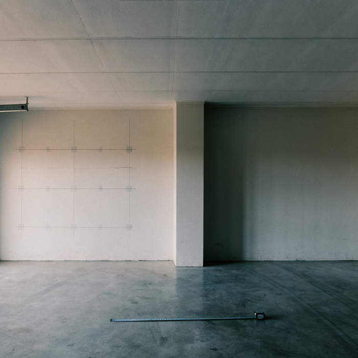 Empty two-car garage with a tape measure on the floor, being measured for a golf simulator