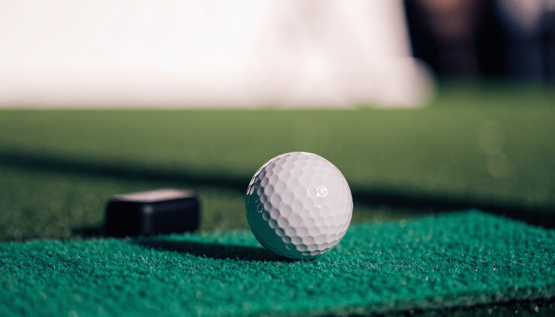 Golf ball on a hitting mat with a launch monitor sensor on the turf behind it