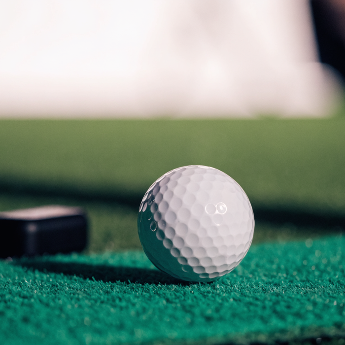 Golf ball on a hitting mat with a launch monitor sensor on the turf behind it
