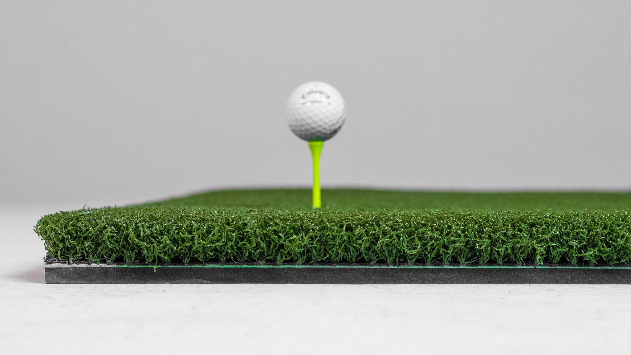 Golf ball on a tee with a green mat and gray background