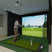Person playing golf simulation game in a home setting with a screen displaying a golf course.